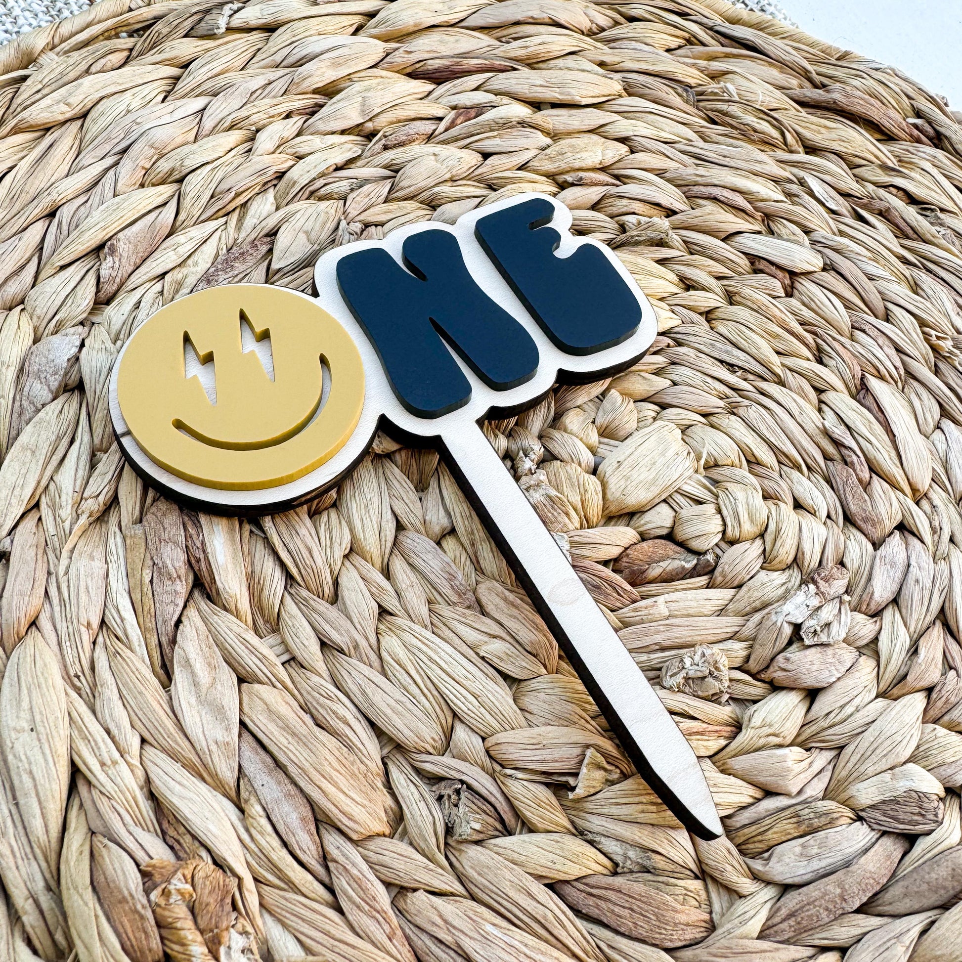 Personalized smiley face first birthday cake topper showing acrylic construction and name