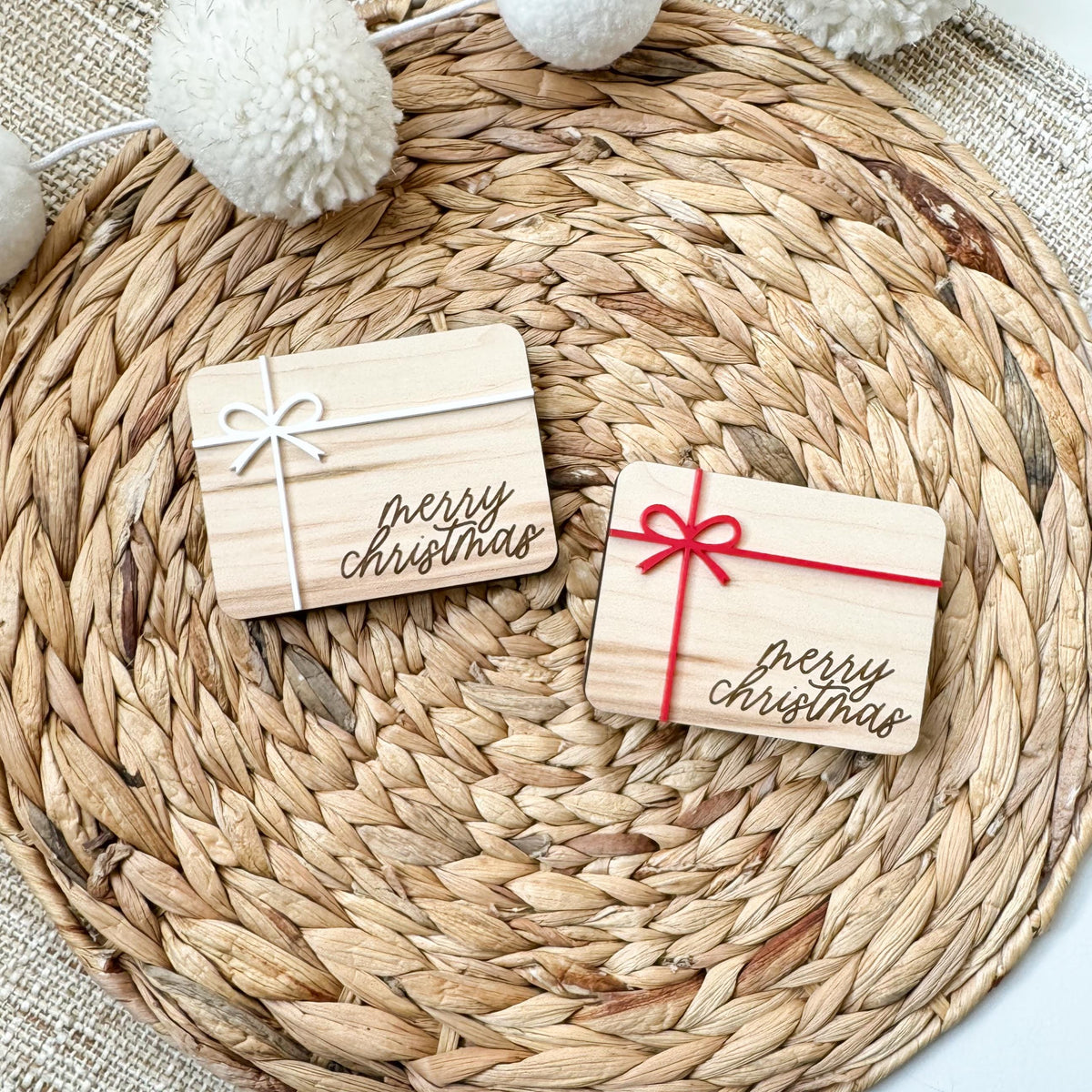 Two wooden Christmas money holders in maple wood with white and red acrylic ribbon and bow and engraved Merry Christmas script, sized for a gift card or folded cash