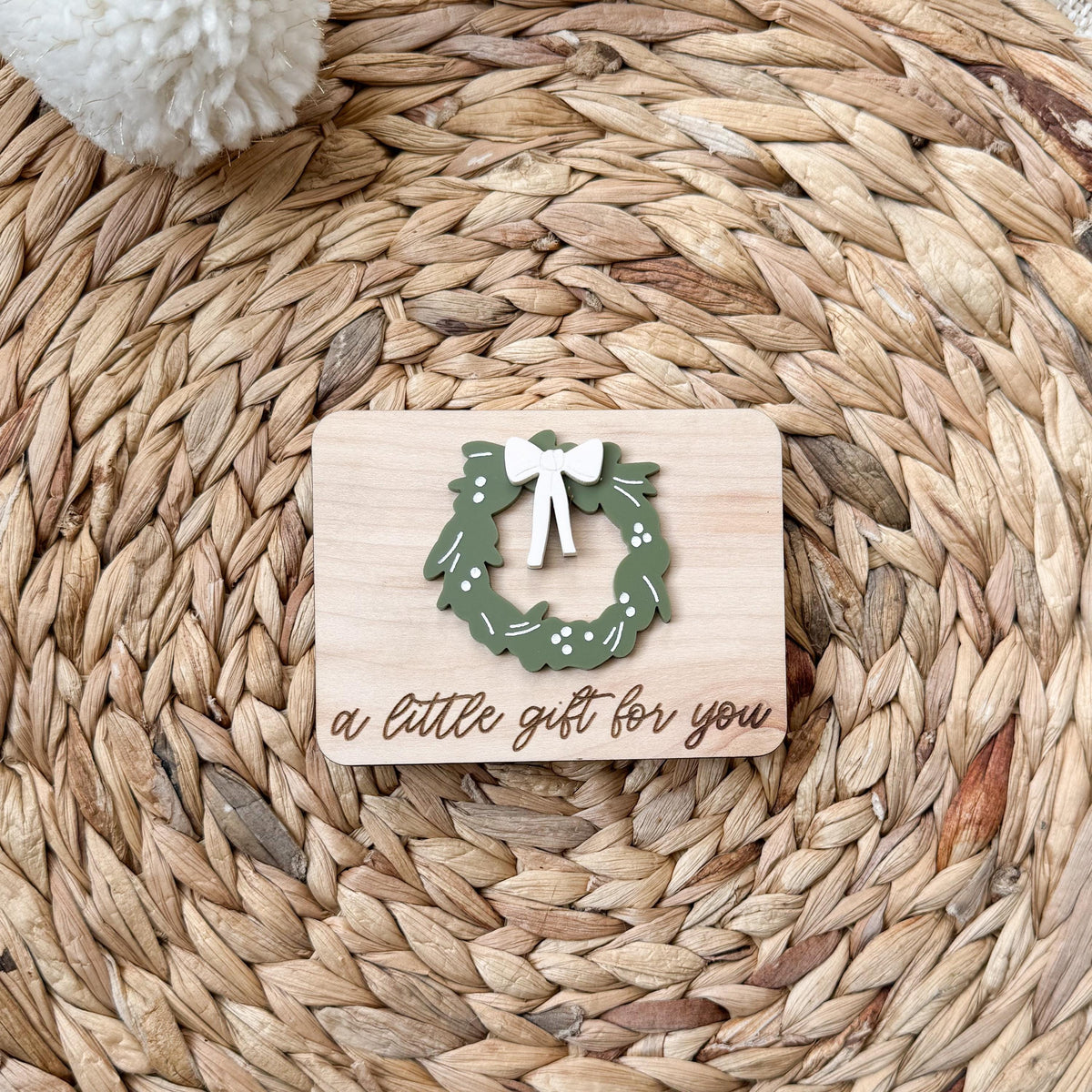 Wreath design money holder in maple wood with a layered green acrylic wreath, white bow, and engraved A Little Gift for You script