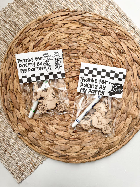 Wooden dirt bike-shaped party favor with “Thanks for Racing By” topper, includes marker and cellophane bag, shown on white background
