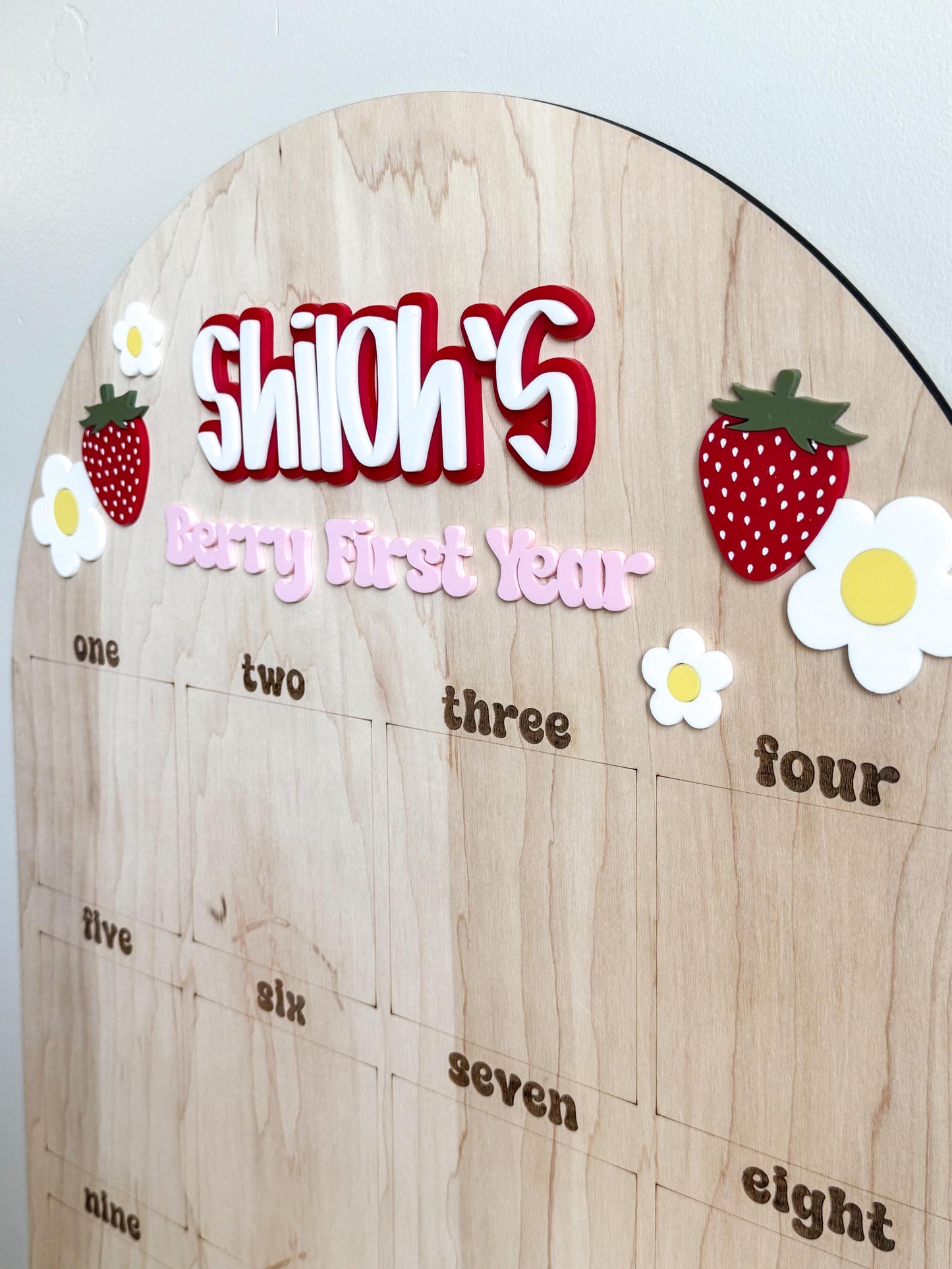 Close-up of berry first birthday photo board in natural maple wood with personalized name