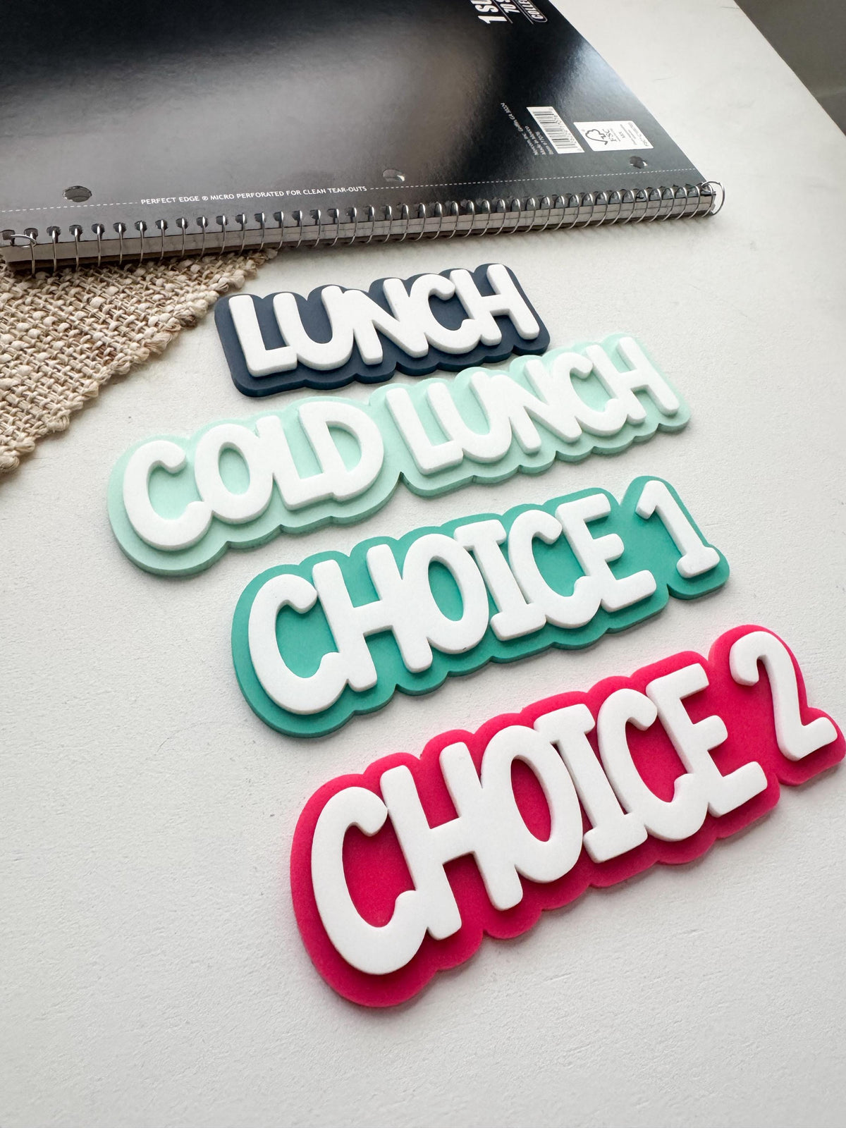 Close-up of layered acrylic lunch choice magnets, Choice 1 in teal and Choice 2 in hot pink with bold white lettering
