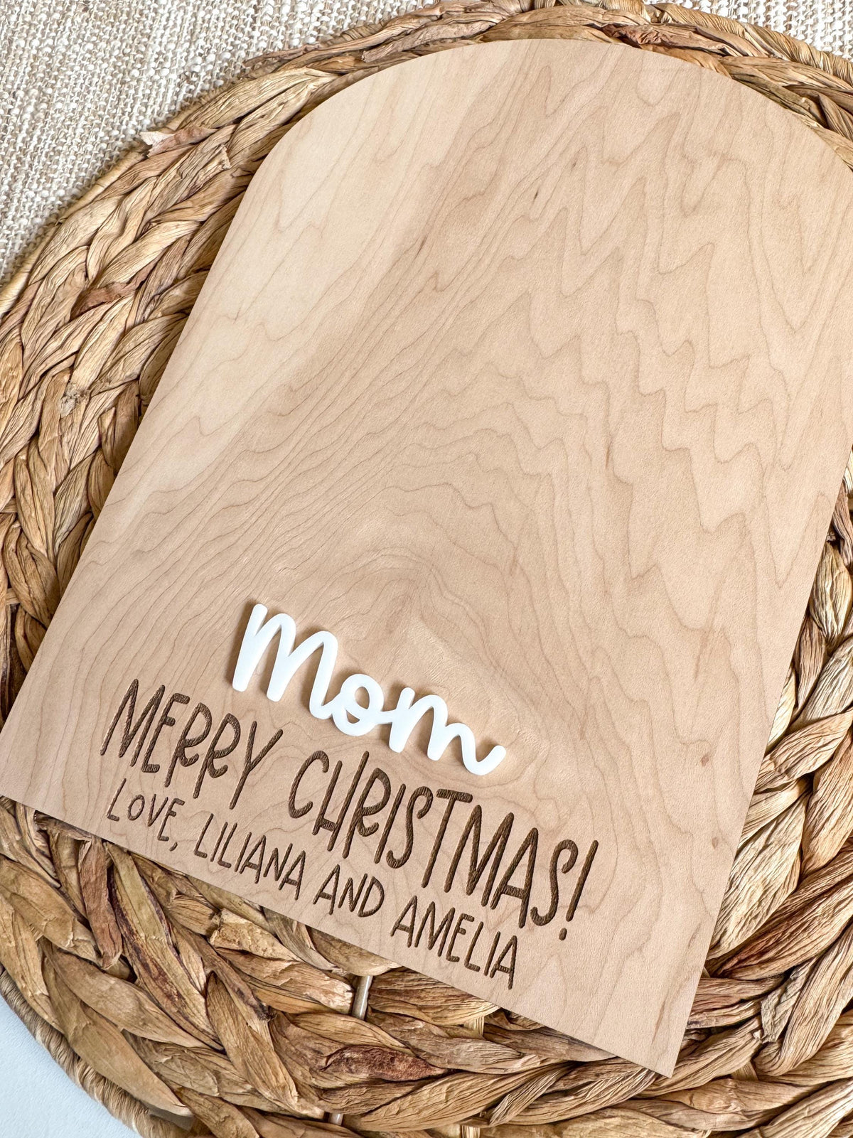 Close-up of the maple wood grain with a raised white acrylic name and laser engraved Merry Christmas message on a personalized handprint keepsake sign