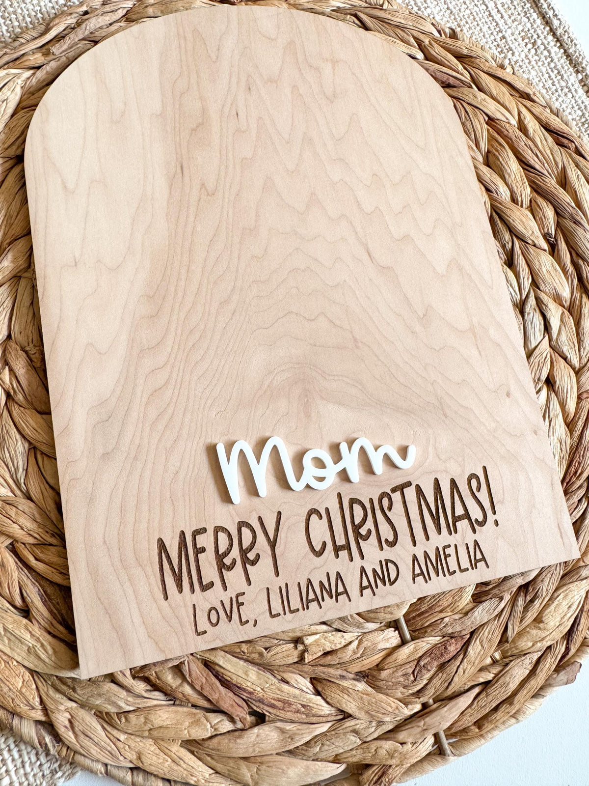 Angled view of a personalized maple wood Christmas keepsake sign for Mom or Grandma showing the smooth arched edge, raised white acrylic name and engraved holiday message