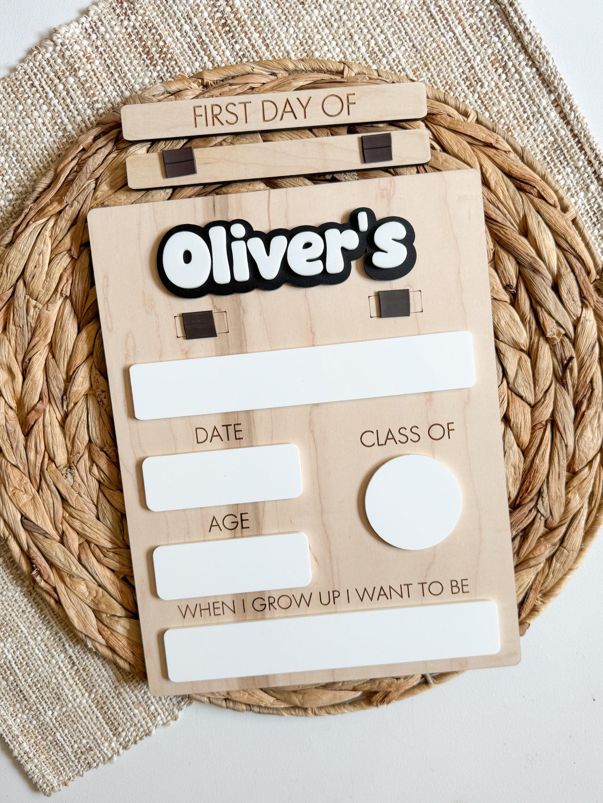 Reusable wooden first day of school sign with blank dry erase spaces for grade, date, age, and future career, displayed on a woven textured background.