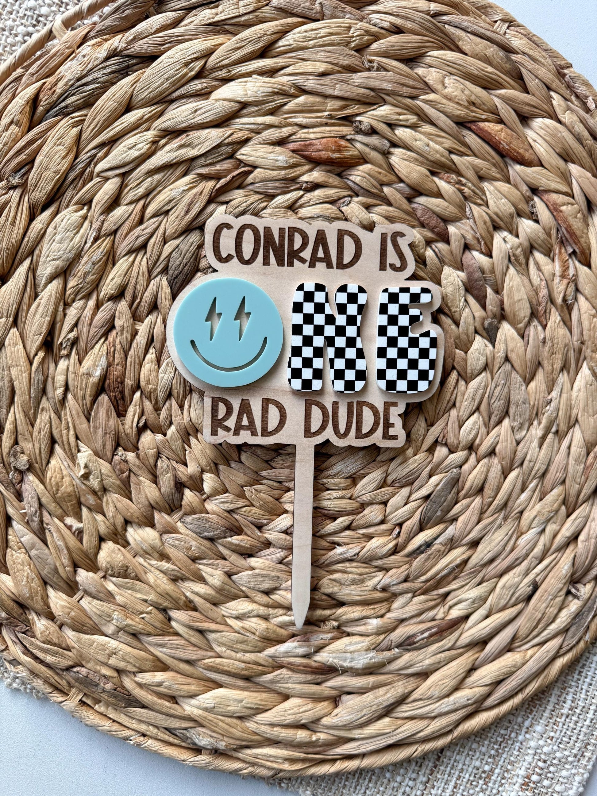 Personalized One Rad Dude 1st birthday cake topper showing checker design and custom name