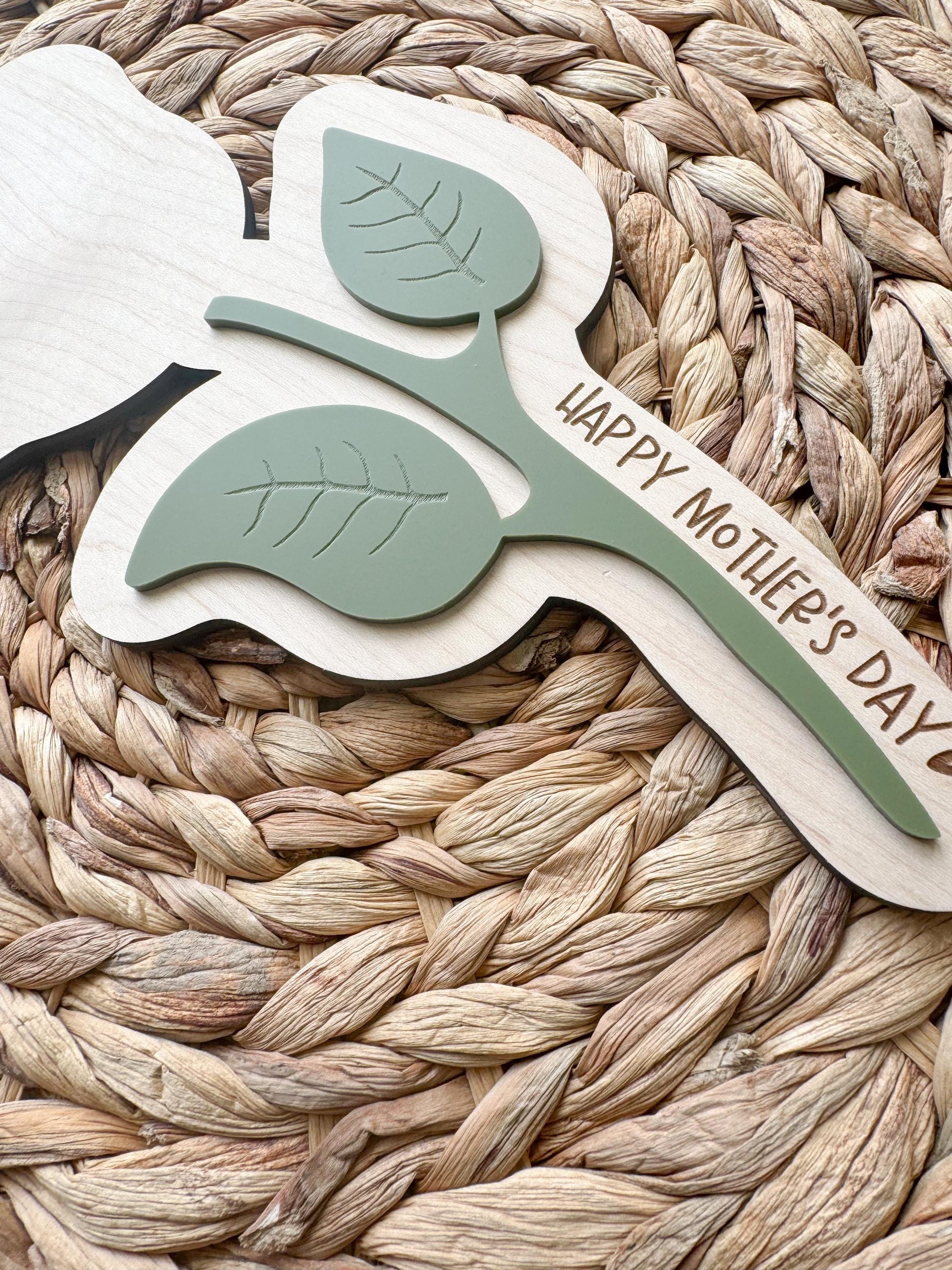 Detail shot of sage green acrylic leaves layered on natural maple wood flower stem with custom Mother’s Day message engraved along the side.