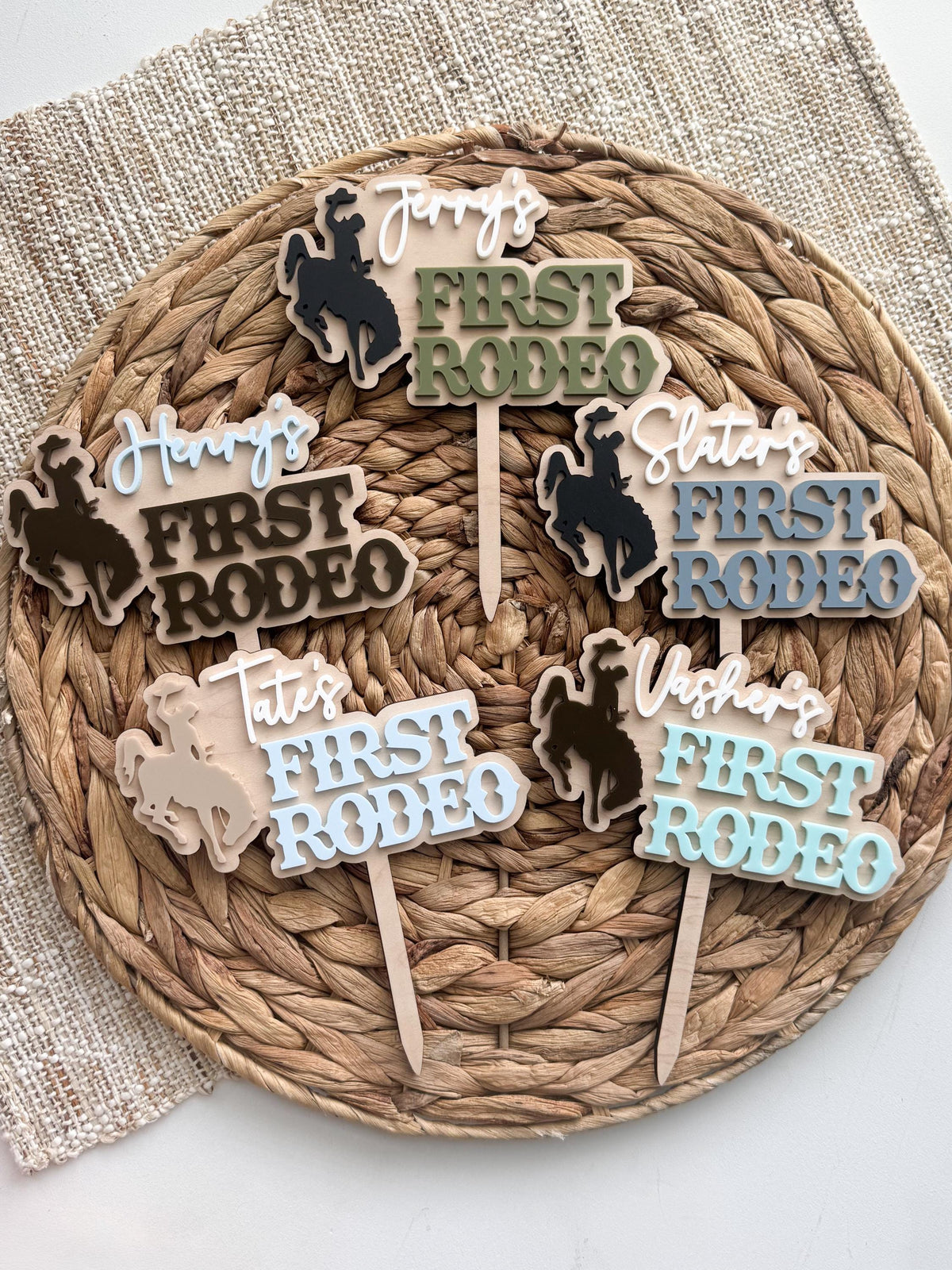 Assortment of personalized western birthday cake toppers showing multiple color options, cowboy and cowgirl silhouettes, and layered acrylic names.