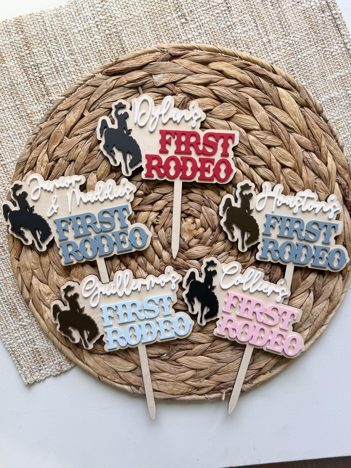 Collection of personalized rodeo cake toppers in multiple acrylic color combinations featuring cowboy and cowgirl bronc rider silhouettes.