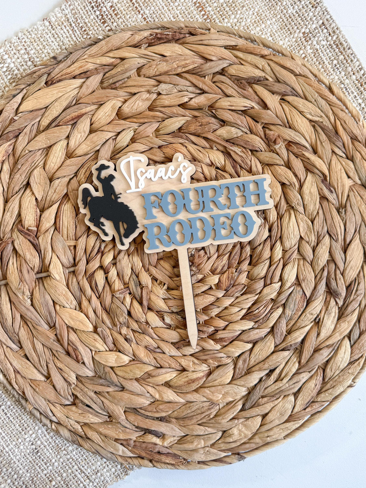 Personalized western birthday cake topper customized for a fourth birthday with layered blue acrylic lettering and cowboy bronc rider silhouette.