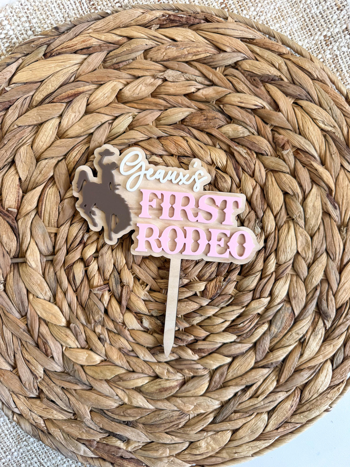 Personalized layered rodeo cake topper with a cowgirl bronc rider silhouette, custom name, pink acrylic lettering, and natural wood backing.