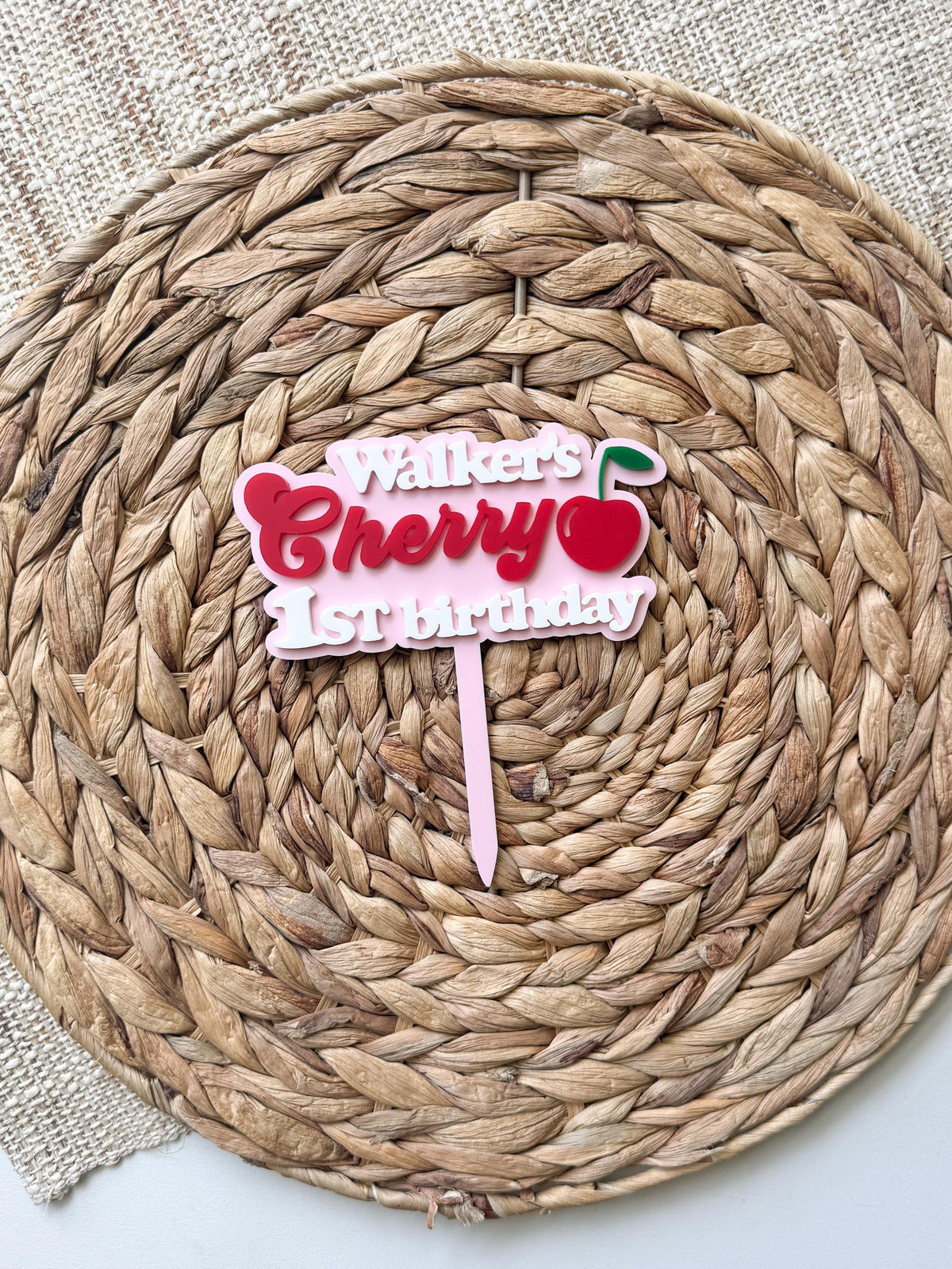 Personalized One Sweet Cherry first birthday cake topper with layered maple wood and pink acrylic on woven background.