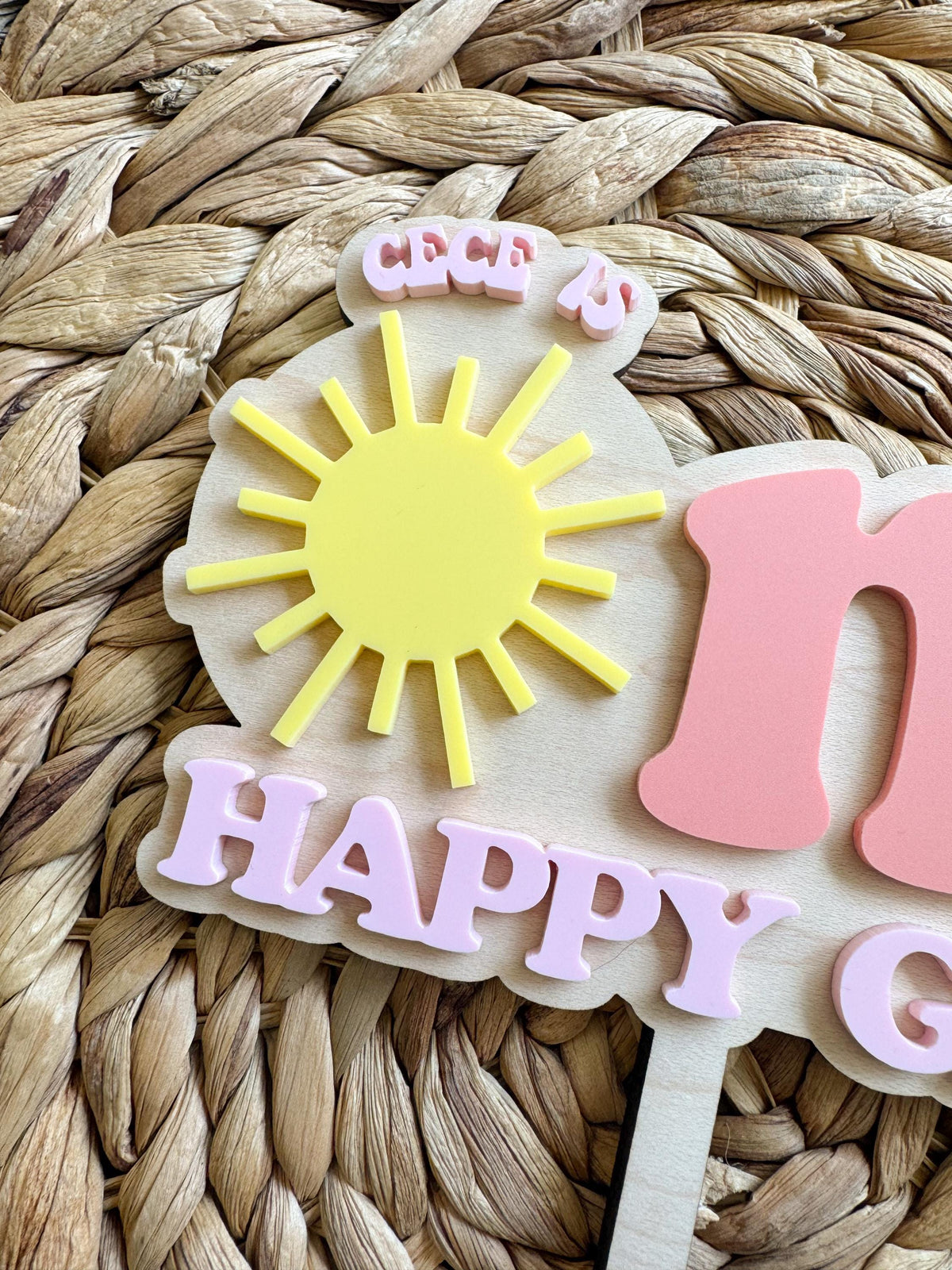Close-up of personalized sunshine first birthday cake topper with custom name and layered acrylic details.