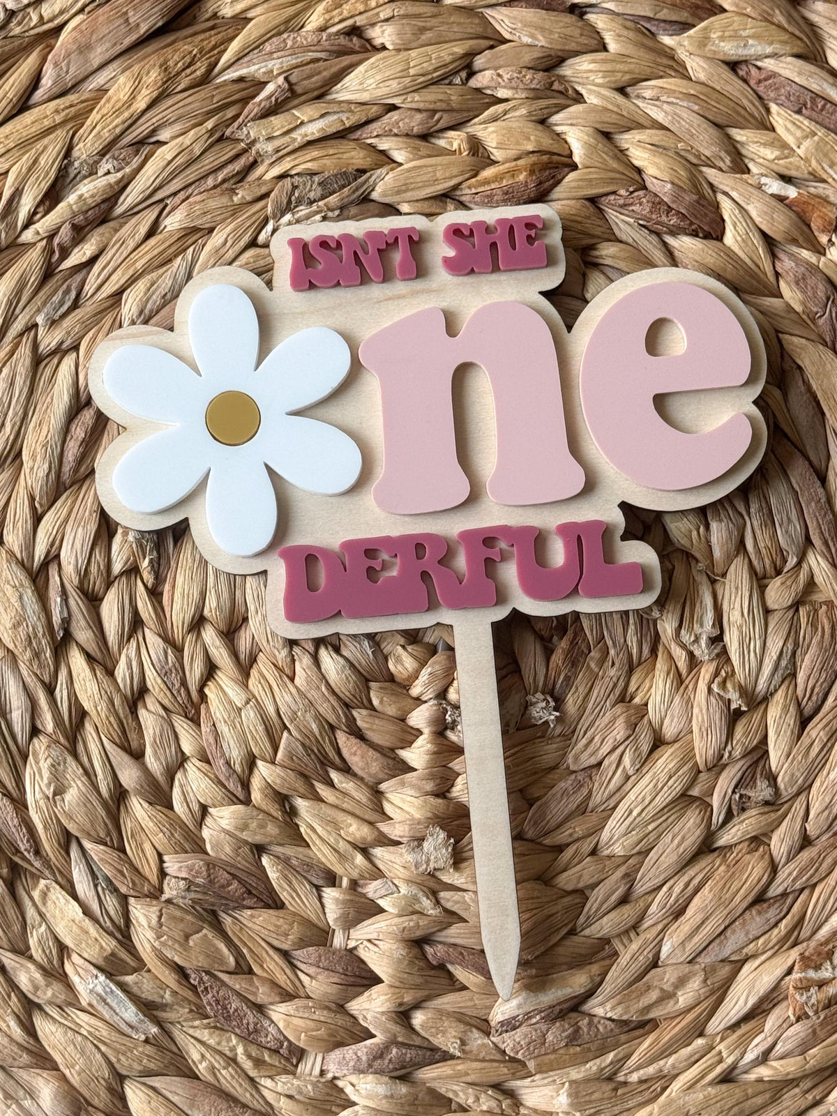 Close-up of personalized first birthday cake topper highlighting layered daisy flower and lettering.