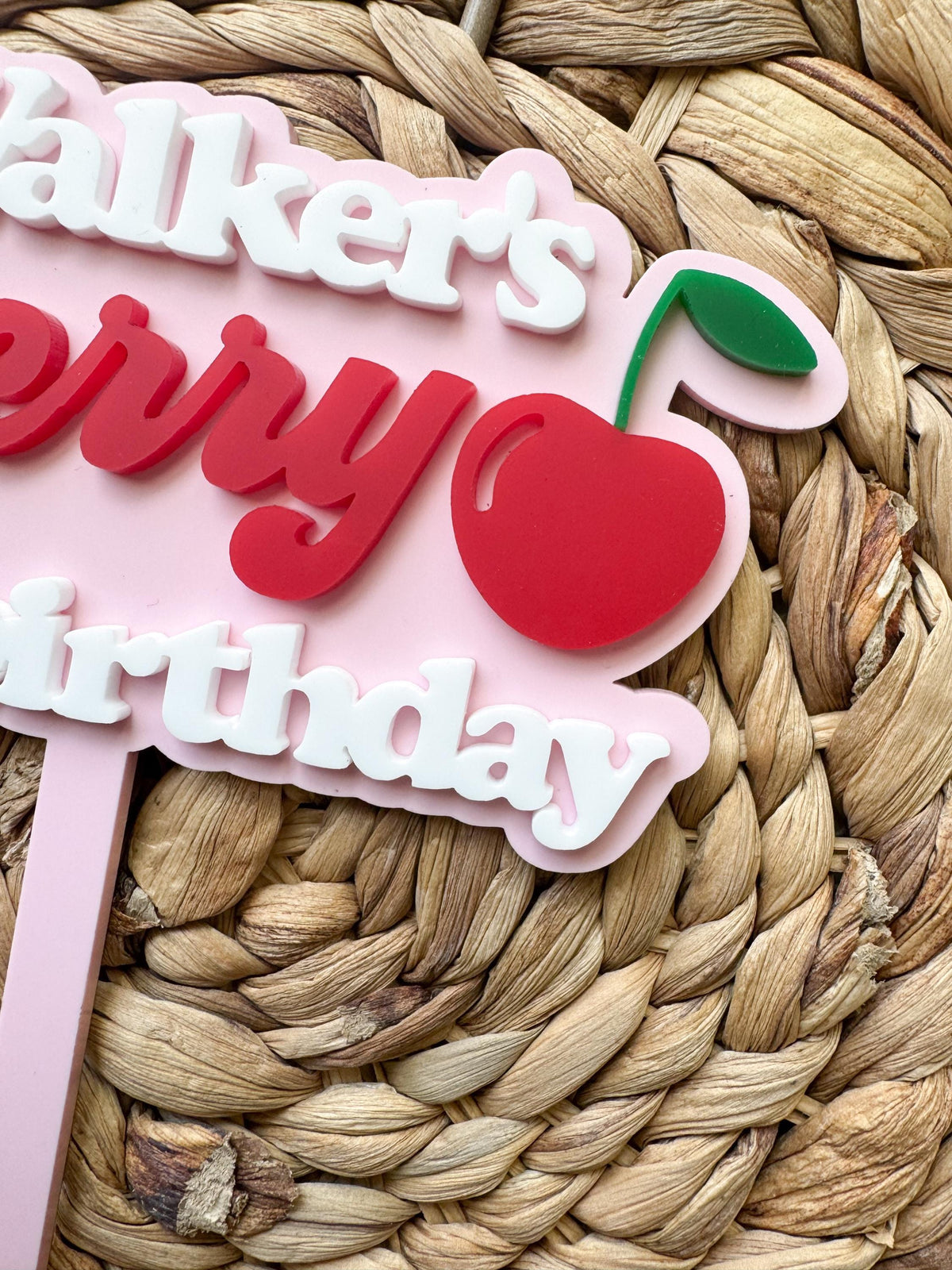 Close-up of red cherry accent and layered acrylic lettering on personalized birthday cake topper.