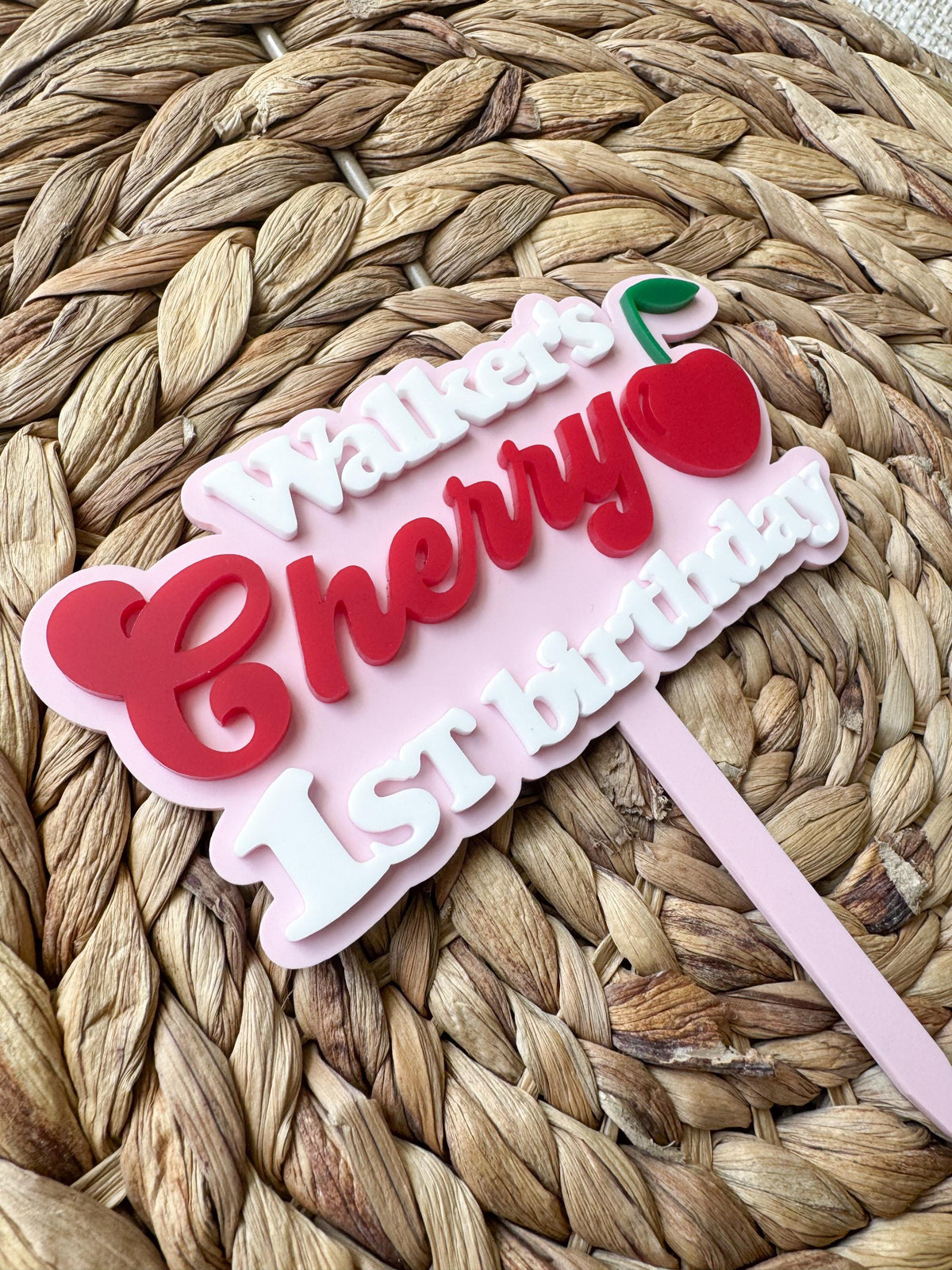 Angled close-up of personalized cherry cake topper highlighting layered acrylic lettering and handmade details.