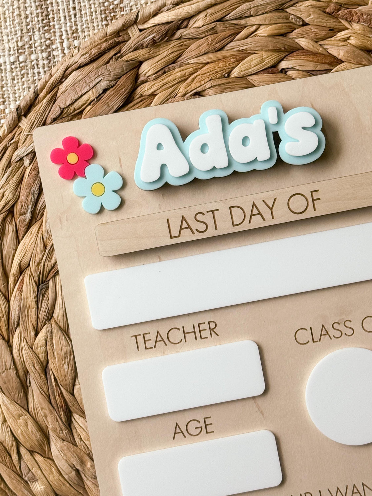 Close-up of personalized back to school sign with blue acrylic name, daisy accents and Last Day Of piece.