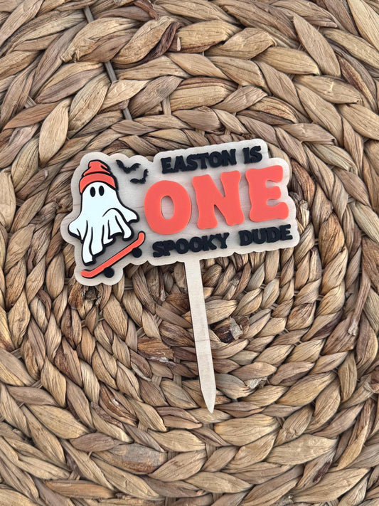 Personalized One Spooky Dude first birthday cake topper with skateboarding ghost, bats, orange ONE lettering and black accents on natural wood.