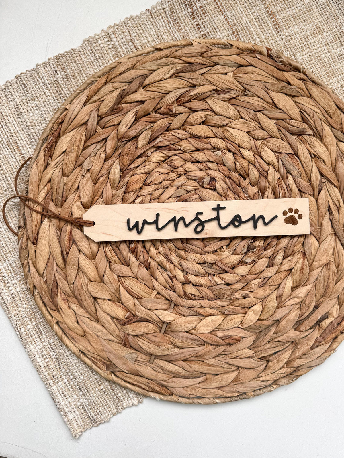 Single personalized pet stocking tag in maple wood with a paw print, shown on a round woven placemat