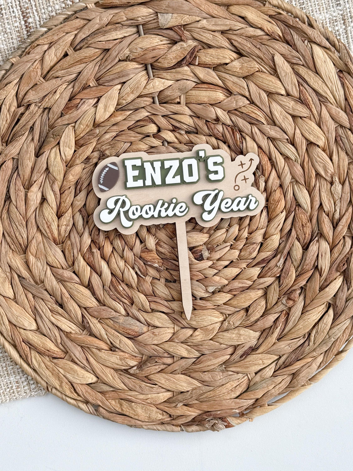 Personalized Rookie Year football first birthday cake topper with child's name, brown football, white and green layered acrylic lettering and natural wood backer.