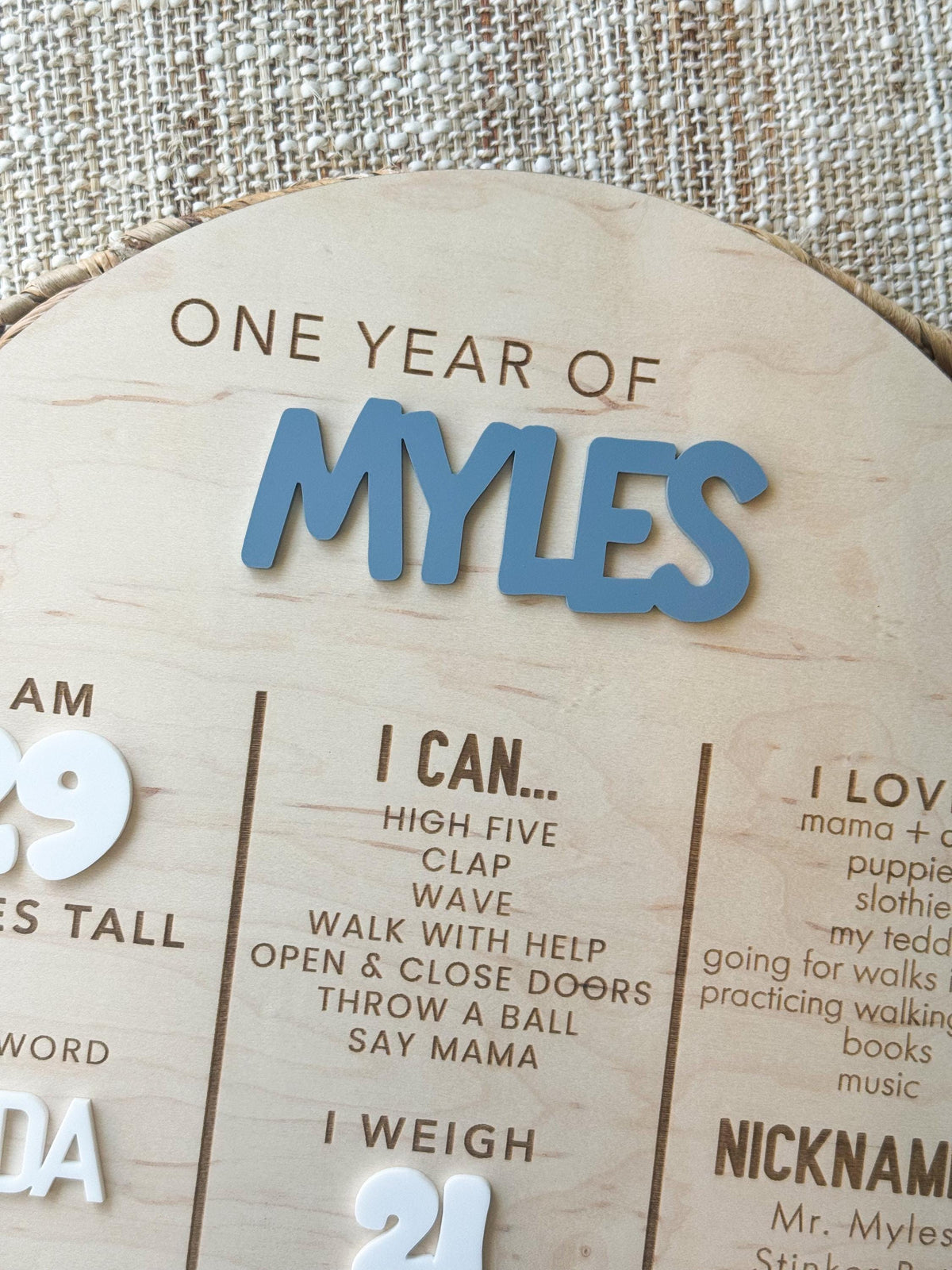 Angled view of the raised blue acrylic name on a personalized first birthday milestone board, showing the dimensional layered finish