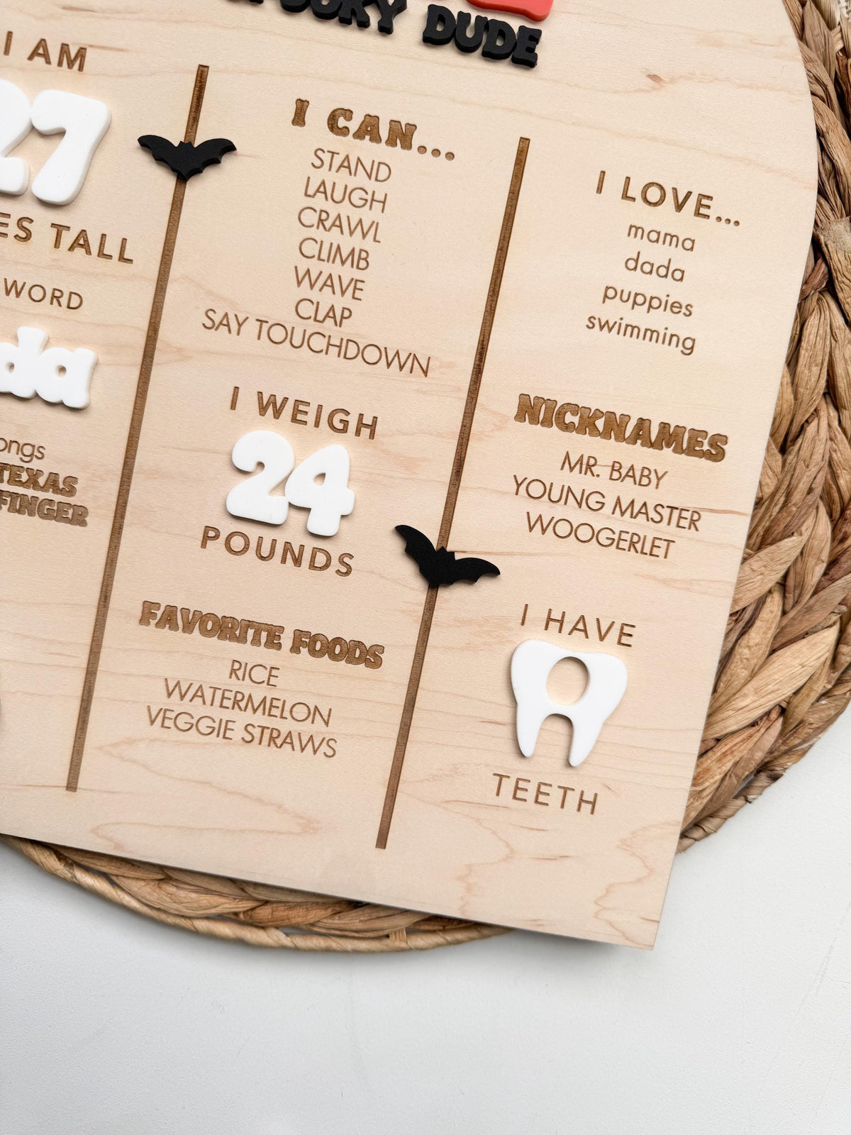 Detail of engraved milestone columns on a personalized baby first birthday board, with I Can skills, I Love list, nicknames, favorite foods, white acrylic weight number, acrylic tooth and black acrylic bats on maple wood.