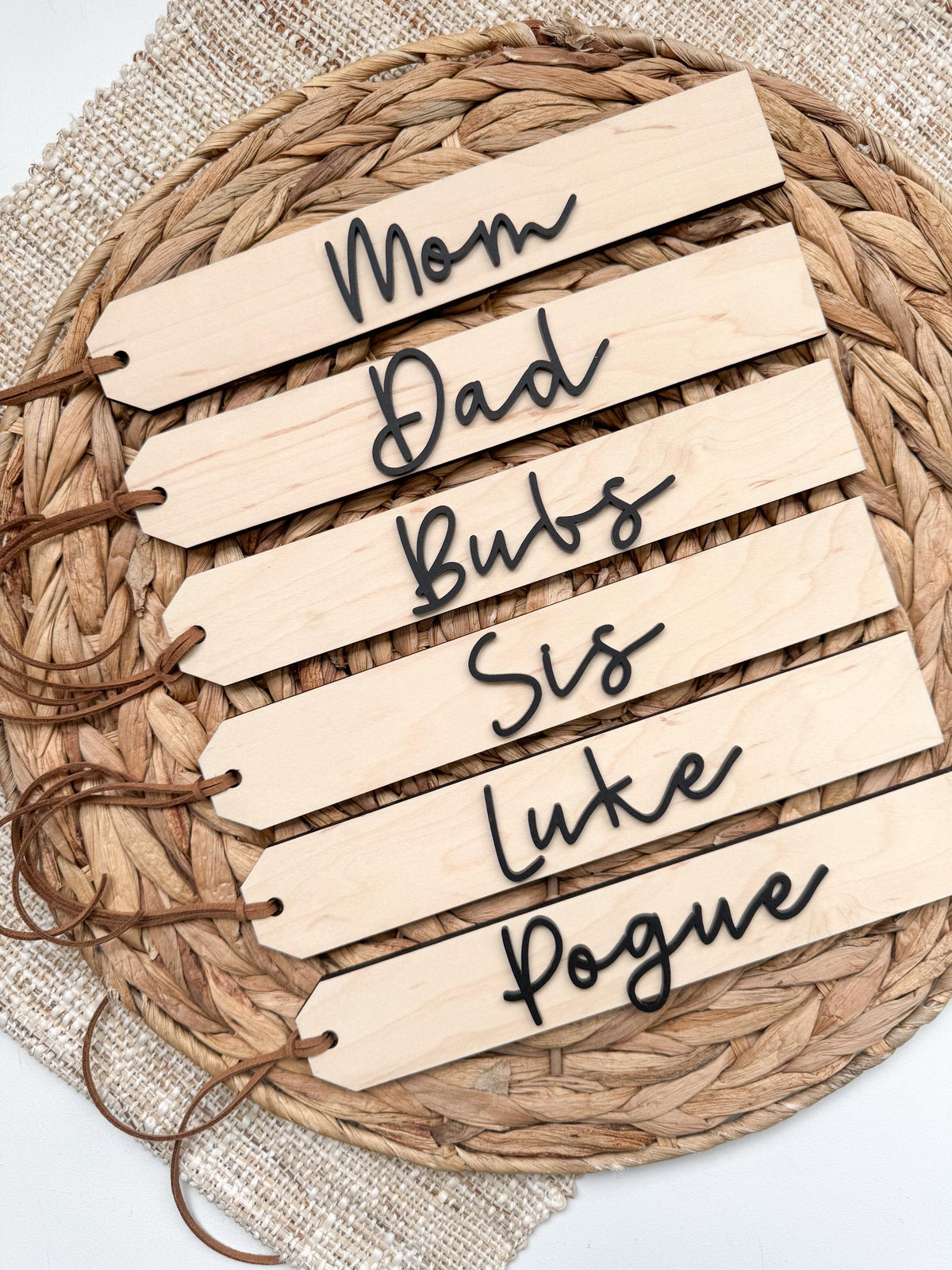 Six personalized wooden stocking tags with family names in script, laid out on a woven placemat