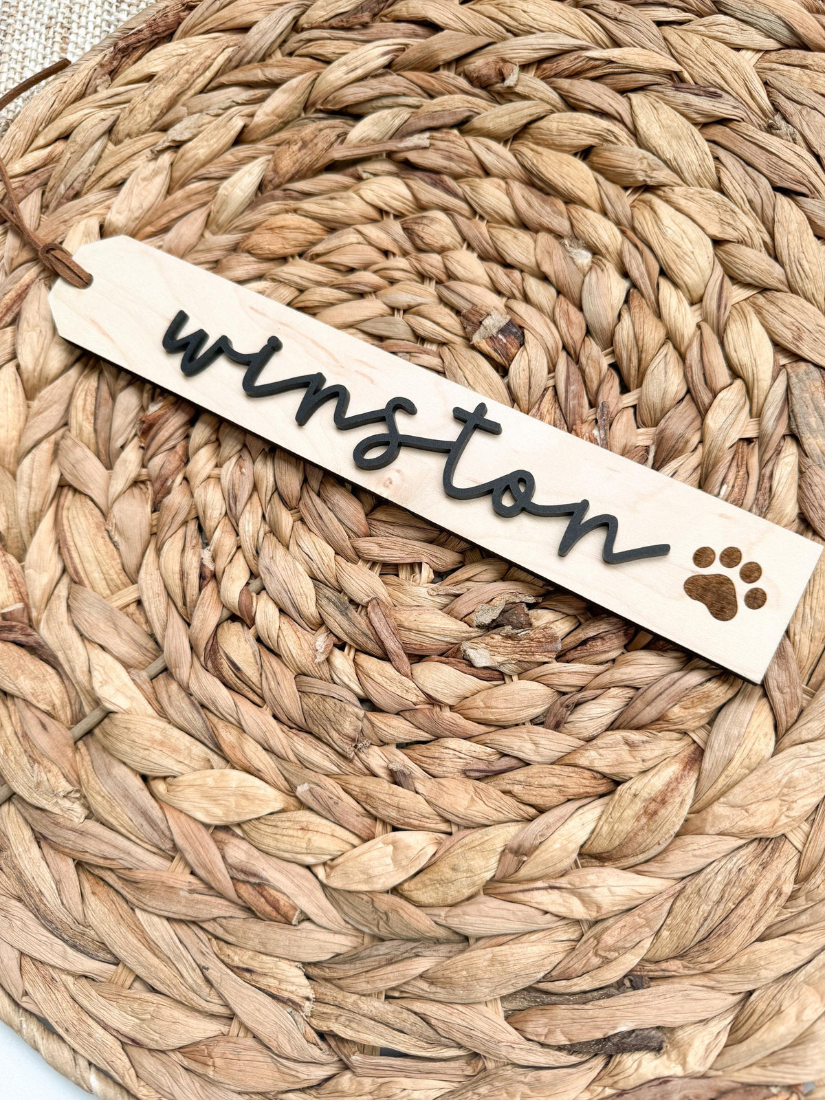 Close-up of a wooden pet stocking name tag with engraved script name and paw print detail