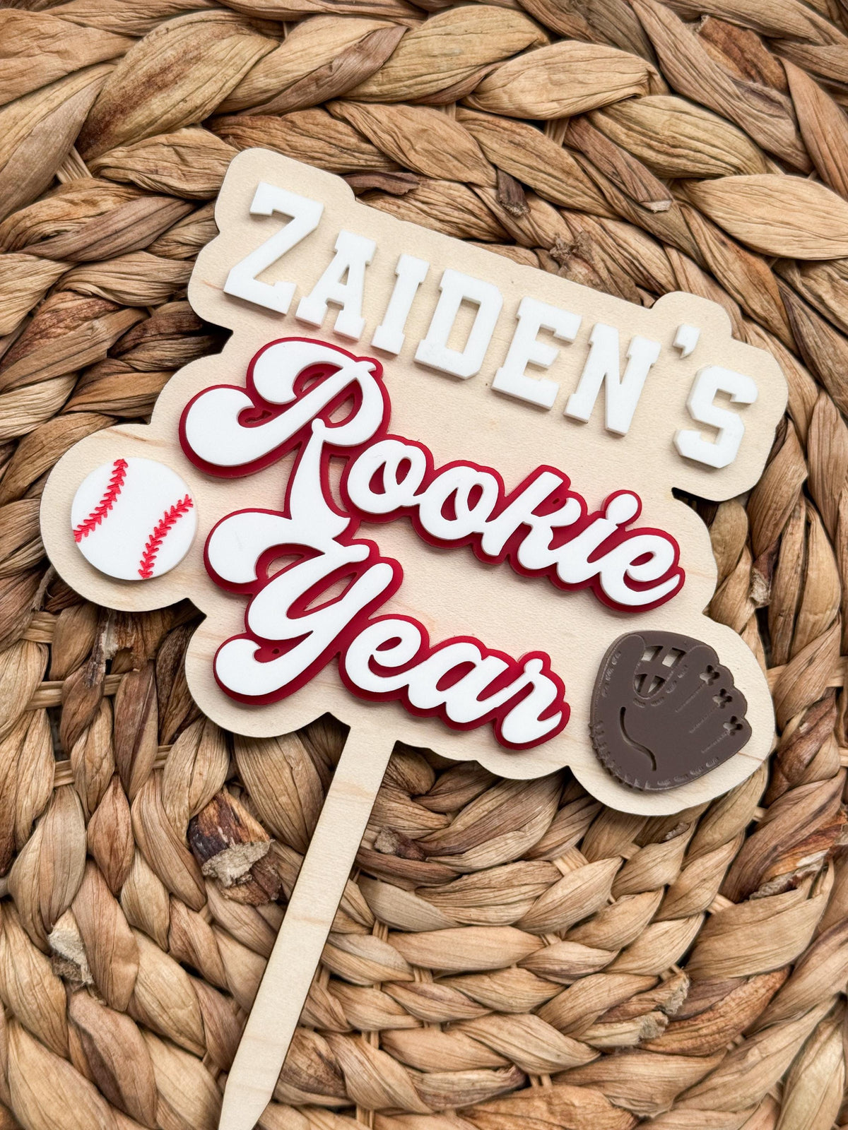 Layered acrylic Rookie Year baseball cake topper with a personalized name in white block letters, red and white script lettering, a baseball and glove on a laser cut maple wood backer.