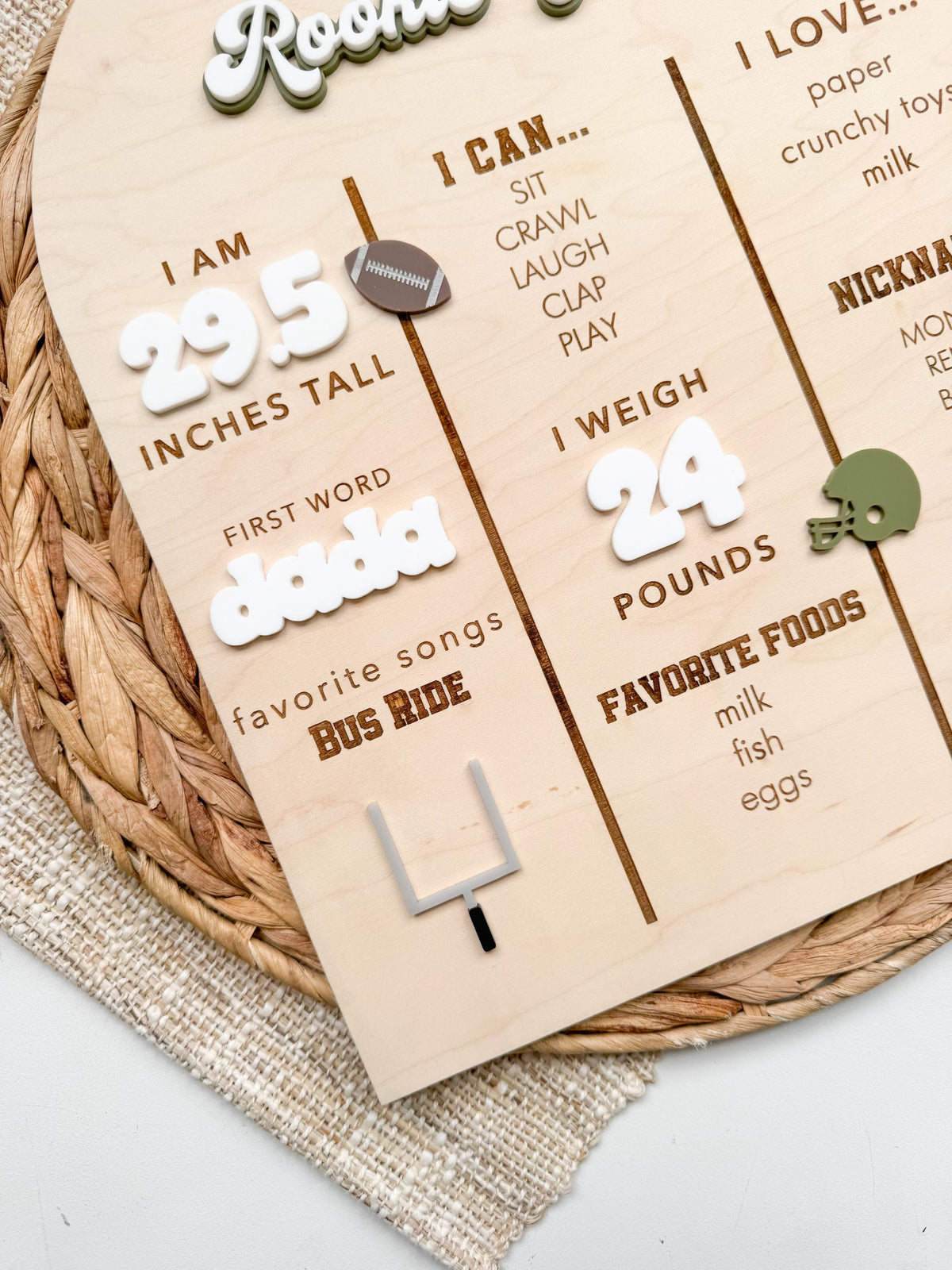 Close view of the left and center columns of a custom football milestone board, with raised white acrylic numbers for height and weight, a laser cut acrylic first word, engraved favorite song and foods, and a layered acrylic goal post on natural maple wood