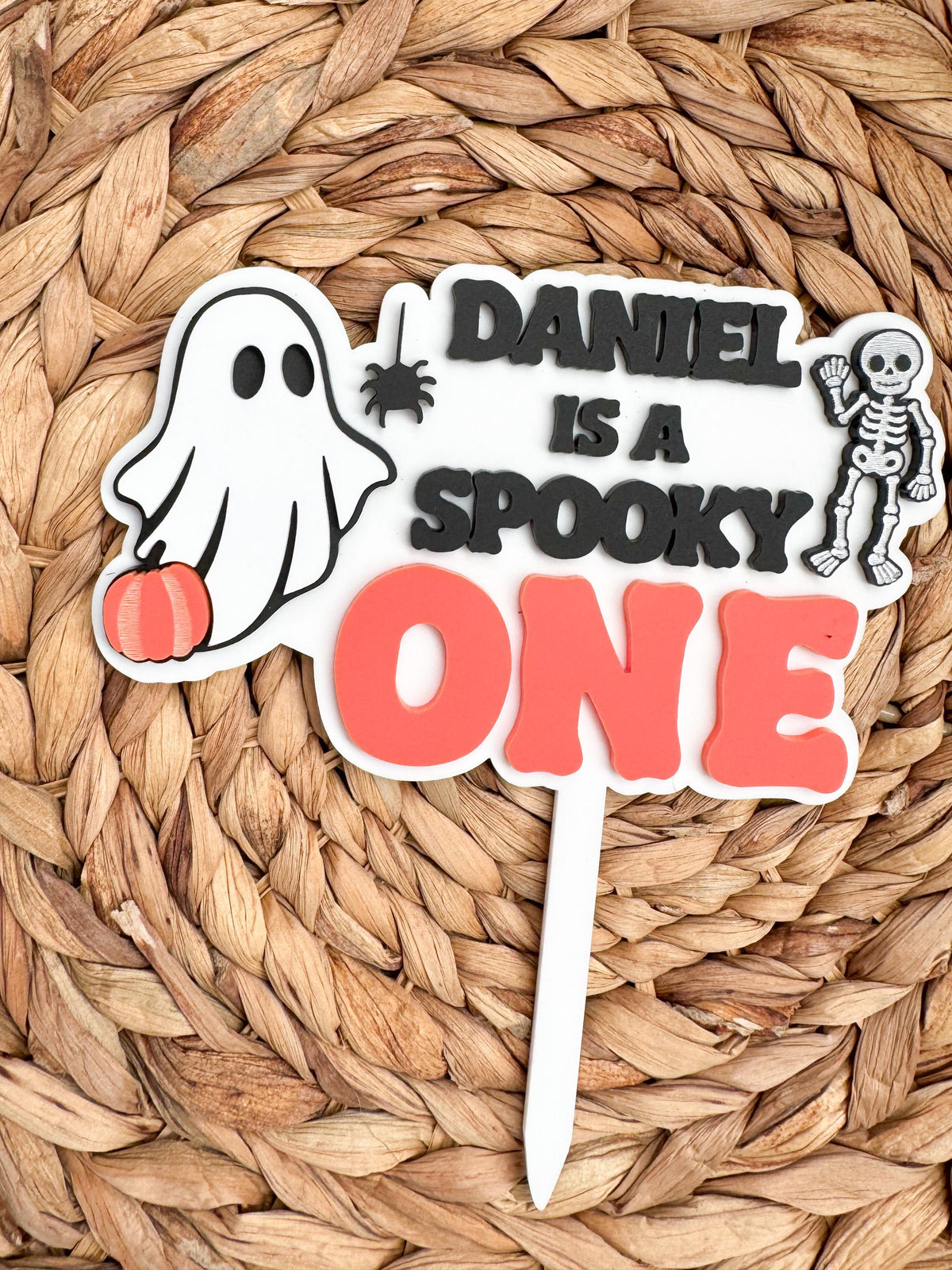 Personalized Spooky One cake topper with a custom name, ghost, pumpkin, spider and skeleton accents for a Halloween 1st birthday party.