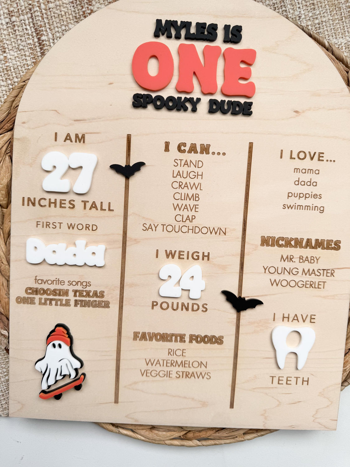 Front view of Halloween first birthday milestone board on maple wood showing engraved I Am, I Can, I Love, I Weigh, favorite foods, nicknames and teeth sections with white acrylic numbers, acrylic tooth and skateboarding ghost accent.