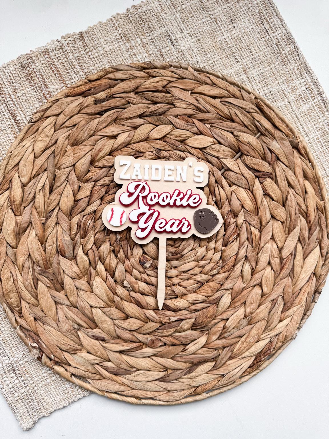 Personalized Rookie Year baseball cake topper for a first birthday, with a custom name, layered white and red acrylic lettering, and baseball and glove accents on a natural maple wood backer.