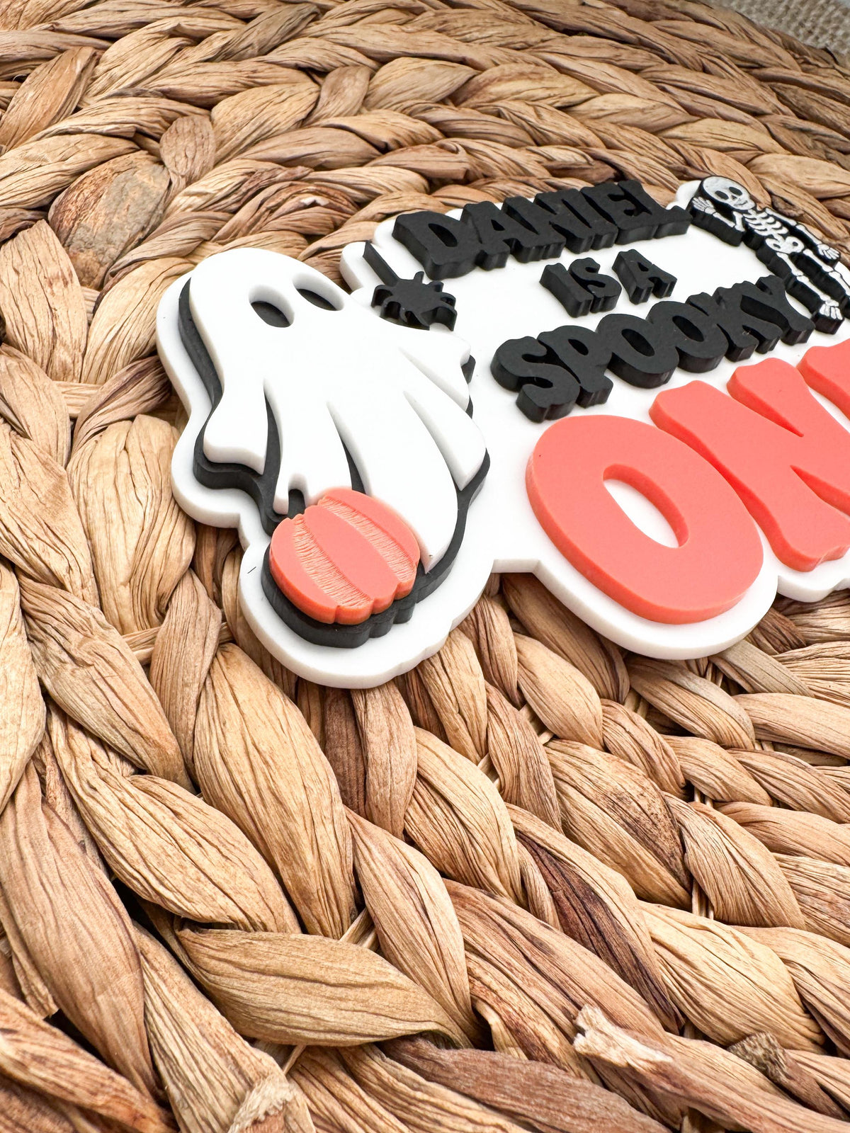 Side view of a personalized Halloween first birthday cake topper showing the dimensional layered acrylic ghost, orange pumpkin and black spider details.