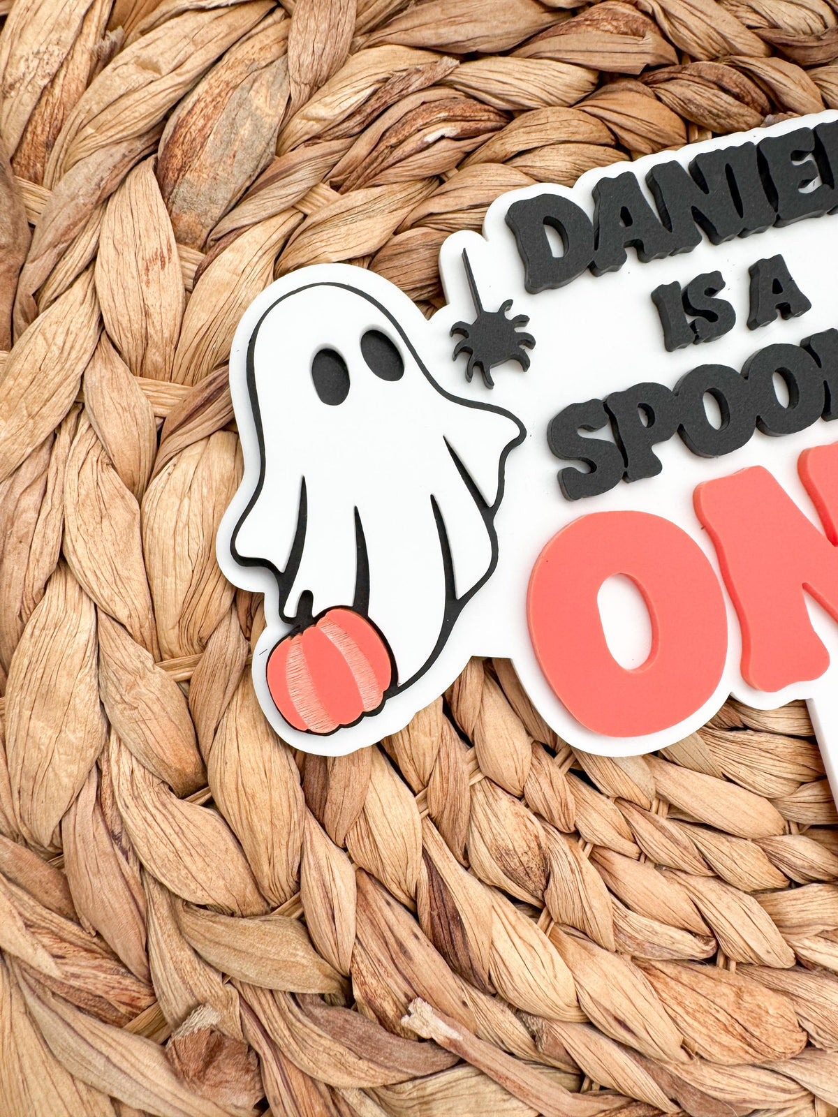 Close-up of a layered acrylic ghost holding an orange pumpkin with a black spider accent on a personalized Spooky One birthday cake topper.