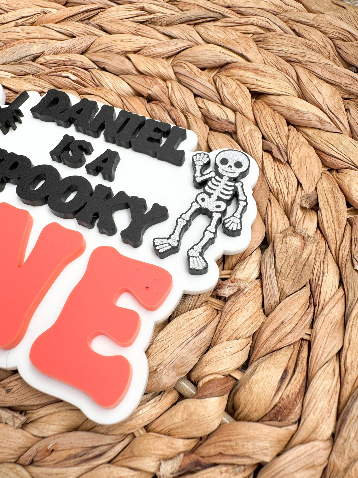 Angled detail of a waving skeleton and bold coral ONE lettering on a custom Halloween first birthday cake topper with raised acrylic layers.
