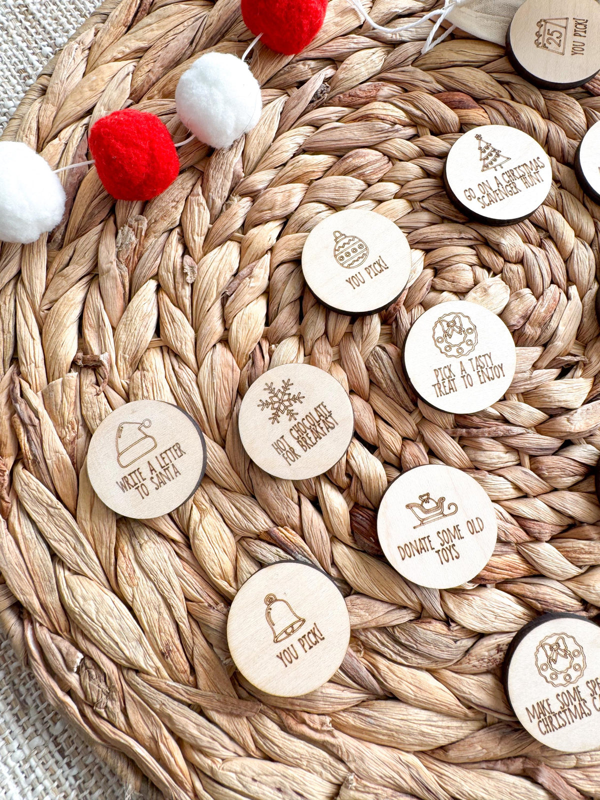Detail of wooden advent tokens engraved with Write a Letter to Santa, Hot Chocolate for Breakfast and a bell You Pick! token. Each 1.5 inch maple coin has a festive icon and a family Christmas activity.